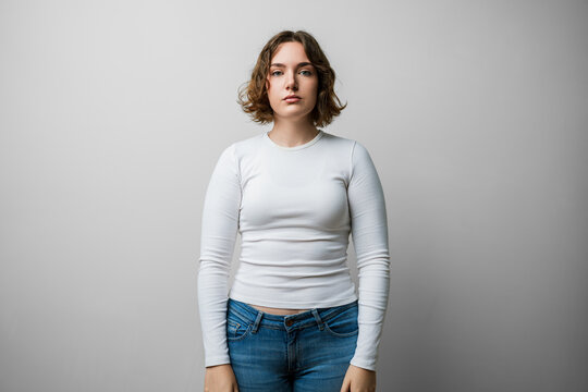 Woman casual portrait, face serious, looking at camera with a natural, simple expression and steady look; confident, thoughtful young person on plain white background