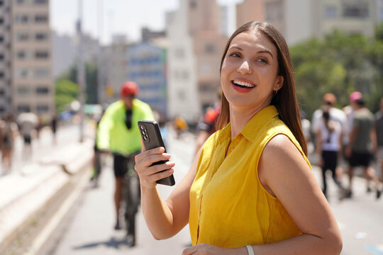 Happy business woman looking away with her smartphone walking on Minhocao pedestrian city street in Sao Paulo, Brazil