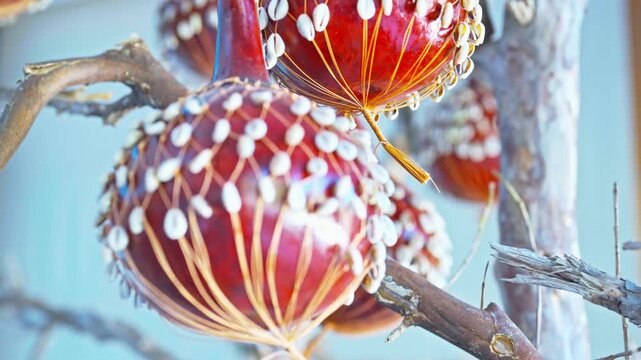 Close-up of traditional handcrafted (calabash) ornaments wrapped in netting and studded with cowrie shells, suspended and gently swaying indoors.