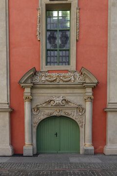View of an ornate historic doorway with a green wooden door and intricate stone carvings set into a salmon-colored building facade in Gdansk, Pomeranian Voivodeship, Poland.