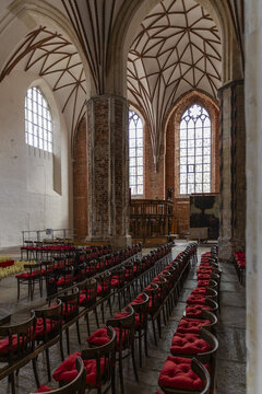 View of the interior of a historic brick Gothic church with vaulted ceilings, tall arched windows, and rows of wooden chairs with red cushions in Gdansk, Pomeranian Voivodeship, Poland.