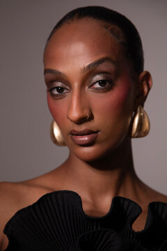 Woman in a black dress with gold earrings on a grey background