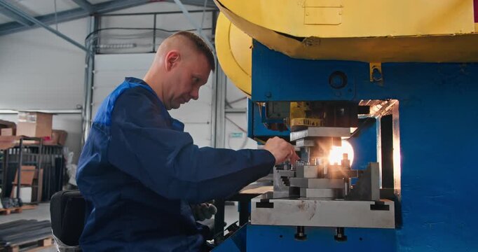 Blue collar machine operator handling metal workpiece at mechanical stamping press. Manufacturing occupation in metalworking industry