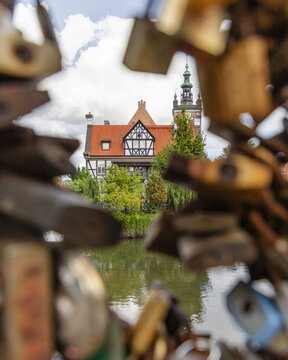 View of a historic half-timbered building with a red roof and tower, framed by love locks on a bridge over a canal in Gdansk, Pomeranian Voivodeship, Poland.