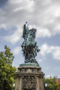 View of the King John III Sobieski Monument, a bronze equestrian statue on an ornate stone pedestal surrounded by lush green trees under a cloudy sky in Gdansk, Pomeranian Voivodeship, Poland.