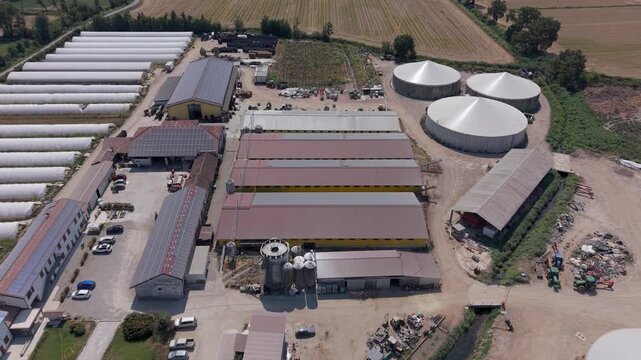 Aerial perspective of biomethane infrastructure integrated with livestock farming, vegetable greenhouses and solar energy systems at a modern agricultural complex in northern Ita