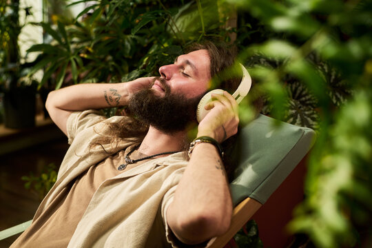 Young adult Caucasian man resting with closed eyes listening to music via headphones. Imagery suitable for mental health awareness, audio streaming ads, mindfulness apps