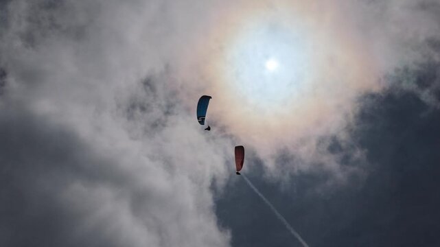 Puy de Dome France two paragliders soaring against bright sunlit clouds, low angle shot extreme sport adventure in dramatic sky.