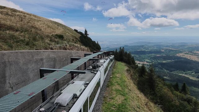 Puy de Dome France Panoramique des Domes rack railway train ascending mountain track, paragliders flying overhead, scenic valley below.