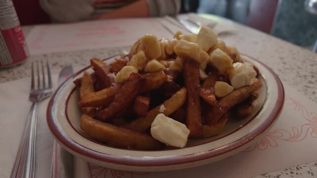 Montreal Canada close up poutine crispy fries piled high with melted cheese curds and gravy, restaurant table setting Quebec comfort food.