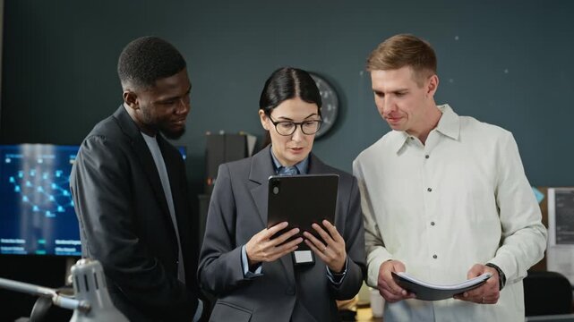 Diverse cybersecurity team including African American man, Caucasian woman, and Caucasian man reviewing data on digital tablet. Ideal for software security marketing and corporate tech campaigns
