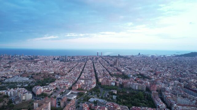Aerial drone slow forward flight from Bunkers del Carmel over Barcelona Eixample grid toward Sagrada Familia and Mediterranean sea, Spain