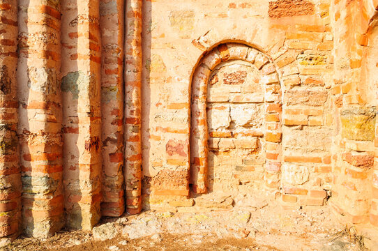 Historic architecture background with a ruined brick wall and a sealed arched opening filled with bricks and rough stones in warm sunlight