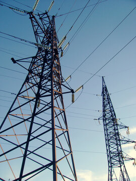 Industrial background with two steel power transmission towers and long cables crossing a clear blue sky with soft white clouds