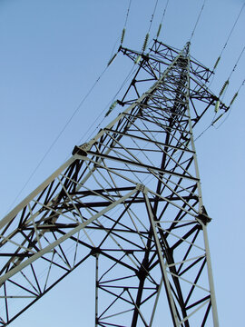 Industrial background with a low angle view of a tall steel power transmission tower and insulators against a clear blue sky above