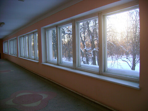 Interior background with a long corridor of large windows overlooking a snowy winter forest and warm sunlight entering the empty hallway