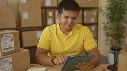 Man taps tablet while surrounded by shipping boxes at a packing desk inside a building  focused entrepreneurship. © Krakenimages.com