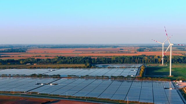 Solar farm and wind turbines at twilight. Aerial perspective depicts photovoltaic panels beside tall wind generators.