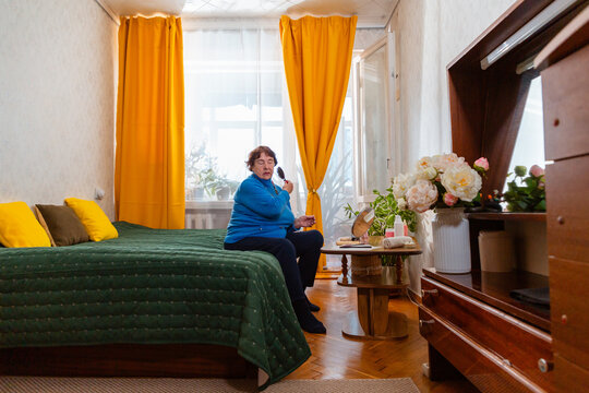 Retired woman applies mascara and lipstick while spending leisure time indoors. Self care and happiness. Wide shot