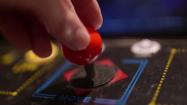 Close up of a hand operating a red joystick on a vintage arcade machine control panel console