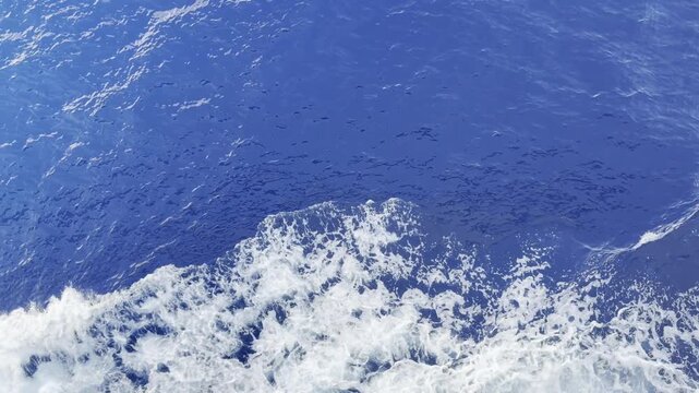 High angle view of white foam from a cruise ship bow wave churning on deep blue Mediterranean Sea water with sun glints