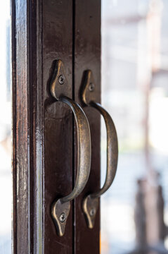 Close-up of vintage brass handles on a dark wooden glass door