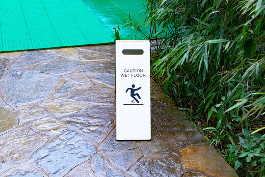 CAUTION WET FLOOR, BEWARE WET FLOOR plastic white board sign. Placed on wet terrazzo walkway. And icon symbol people warning message about someone slipping and falling.