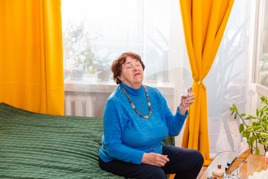 Retired Caucasian grandmother applying perfume while relaxing at home. Her daily beauty routine reflects self care, personal attention, confidence, and the importance of enjoying life after retirement