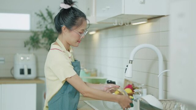 Young Asian Woman Washing Glass Jar with Sponge at Kitchen Sink in Modern Domestic Kitchen
