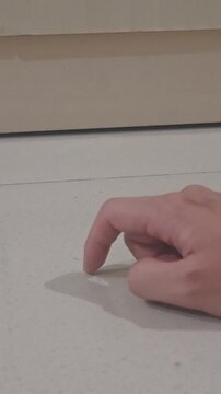 a person's hand with a bent index finger tapping rhythmically on a smooth, clean tile floor, casting a distinct shadow. Concept image representing impatience, waiting, anxiety, boredom