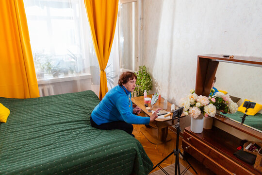 Elderly Caucasian woman enjoying a cosmetic routine while relaxing on a bed. Personal care and attention to appearance represent beauty, confidence, independence, and comfortable retirement. Wide shot