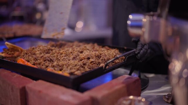 Professional chef cooking shredded meat on a large flat griddle at a catering event buffet station
