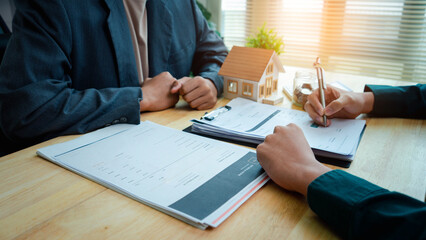 Real estate agen reviewing and signing property documents beside a model house and savings jar, illustrating real estate contracts, mortgage planning, home purchase, and property investment. © ภาคภูมิ ปัจจังคะตา