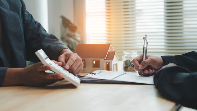 Real estate agen reviewing and signing property documents beside a model house and savings jar, illustrating real estate contracts, mortgage planning, home purchase,  and property investment.