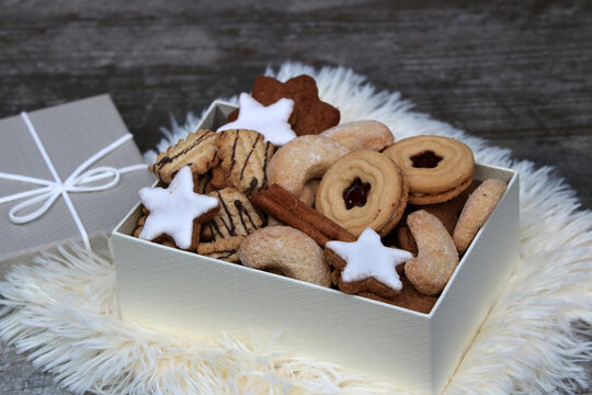 Keksschachtel mit verschiedenen traditionellen Pl&auml;tzchen wie  zimtsterne, vanillekipferl, spitzbuben,  und linzer augen auf wei&szlig;em Fellhintergrund.