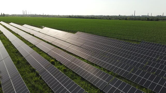 Solar panels farm producing renewable sun energy with industrial cityscape on the horizon, aerial view