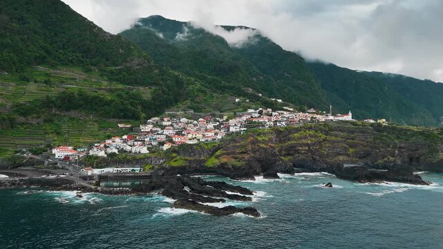 Seixal coastal village in Madeira, Portugal, aerial view from ocean. Forested mountains rise behind settlement on rugged north coast