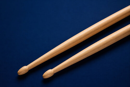 Two wooden drumsticks are resting on a dark blue surface.
