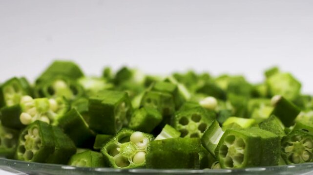 Fresh chopped okra pieces rotating on glass plate against clean white background in studio lighting.