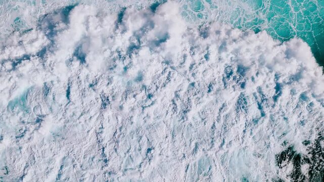 Top down view of ocean waves breaking into dense foam, forming a dramatic natural water background