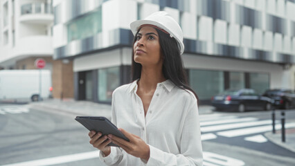 Woman architect in hardhat holds tablet and looks up at building, assessing facade  focus competence. © Krakenimages.com