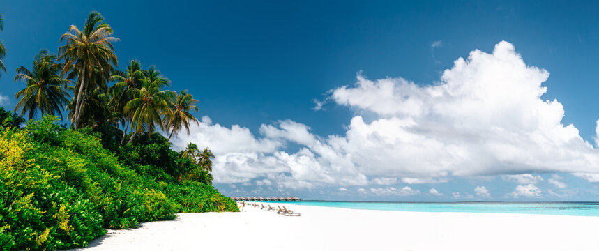 Panoramic view of tropical beach with white sand, palm trees, turquoise ocean water and blue cloudy sky