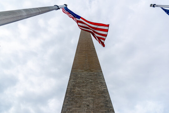 Washington Monument viewed from below with American flag under overcast sky