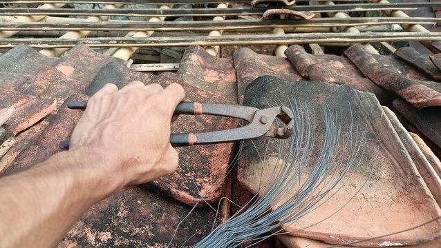 hand holding pincers pliers with binding iron wire for clay tile roof repair work