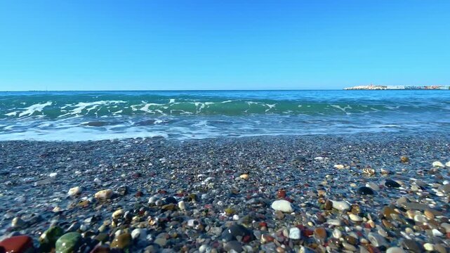 Waves breaking on a pebble beach under a clear blue sky