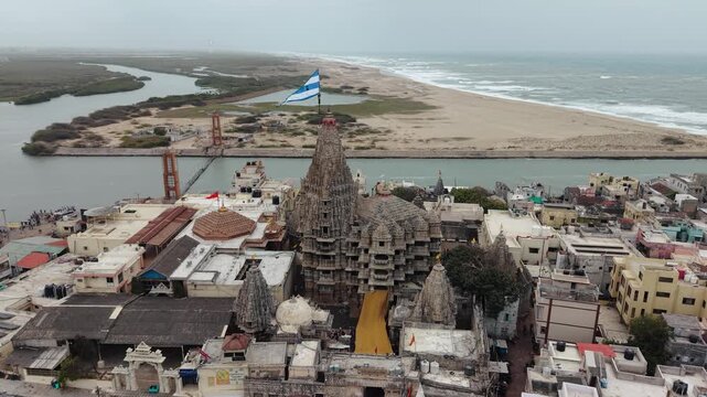 High-angle aerial drone footage capturing the ancient Dwarkadhish Temple (Jagat Mandir) with its iconic flag fluttering atop the spire in the holy city of Dwarka, Gujarat, India.