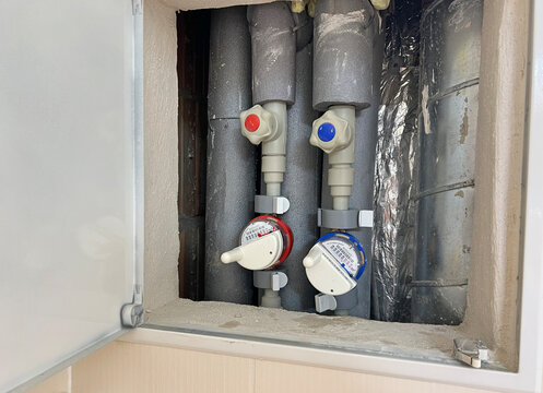 Hot and cold water meters with IoT remote reading modules, valves and insulated pipes installed inside a residential plumbing service cabinet.