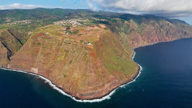 Westernmost headland of Madeira with Ponta do Pargo lighthouse above Atlantic Ocean, Portugal. Broad aerial landscape of coastal escarpment and hillside settlement