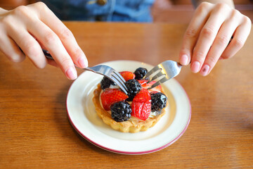 Female hands with forks and cake with berries on table with juice in cafe - Hands hold forks above a berry tart. Fruit rests on a golden, flaky base. Plate sits on a wooden table surface © Pavel Losevsky