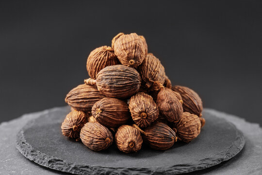 black cardamom seed pods on a black slate stone tray